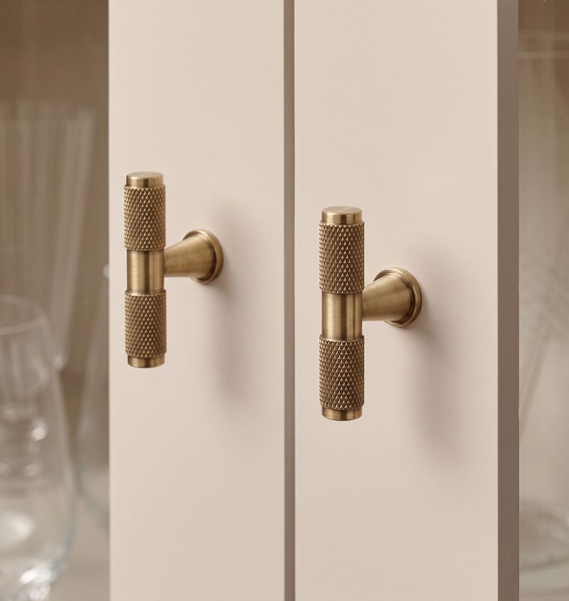 A curved oval cabinet handle in golden brass from the Hometouch collection, featured in a minimalist product photograph for use in furniture hardware catalogs and kitchen renovation visualizations.