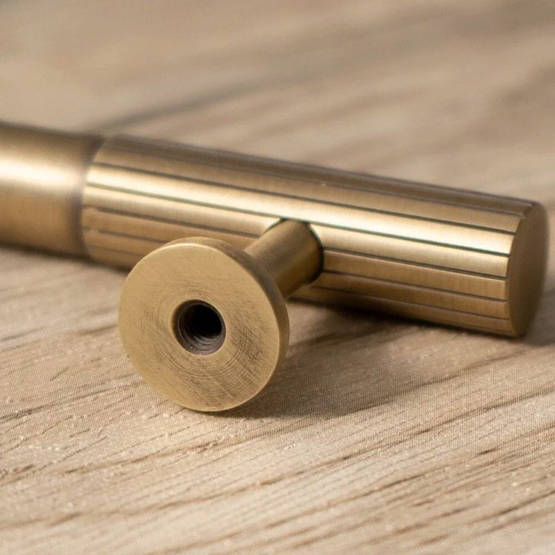 An antique brass-finished oval cabinet pull bar from Hometouch's hardware collection, presented in clean product photography for use in furniture design specifications and e-commerce contexts; source details available at www.hometouchware.com.