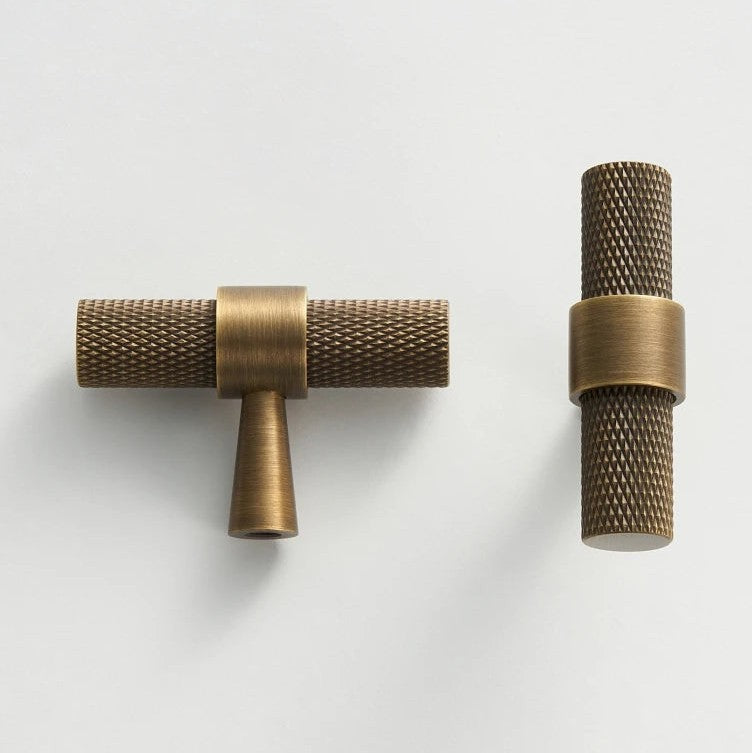 A textured brass dual t-bar door pull handle from Hometouchware photographed against a neutral background, showcasing the product's matte metallic finish and symmetrical linear form for architectural hardware specification or interior design visualization. www.hometouchware.com