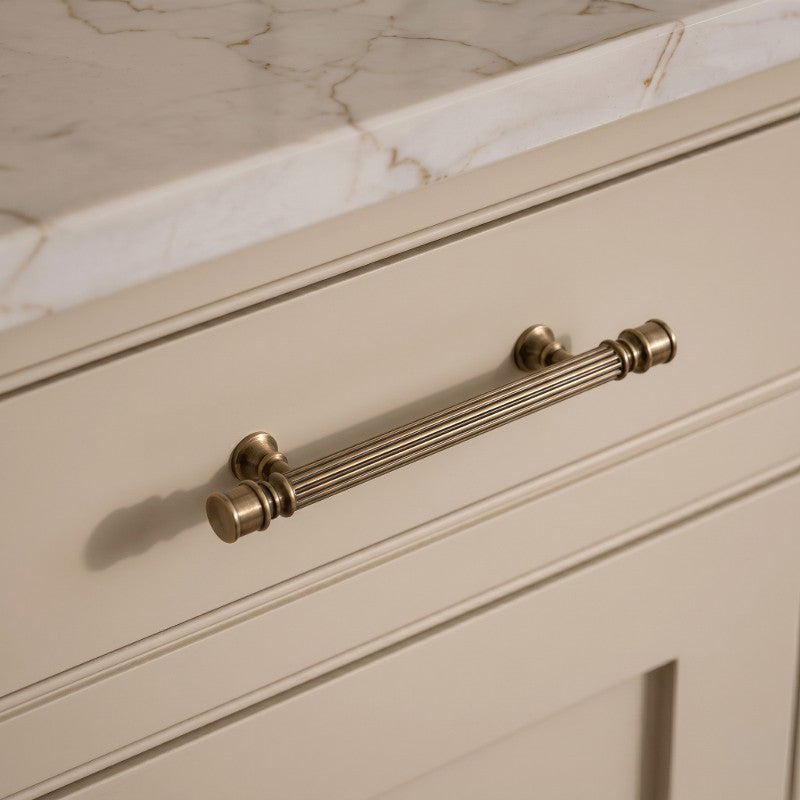 Textured ribbed brass drawer pull in modern European style, elegantly mounted on a cream kitchen cabinet by HomeTouch.